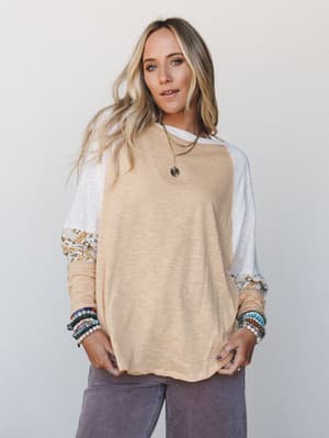A relaxed color-block long-sleeve top in warm sand and white with a patterned mixed-print sleeve panel, styled with wide-leg mauve pants and layered boho jewelry for an effortlessly lived-in look.
