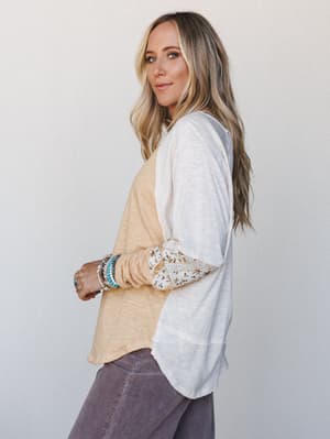 A relaxed colorblock long-sleeve top in warm mango and cream, styled with dusty mauve corduroy pants and a stack of turquoise and silver bracelets — the kind of effortless everyday outfit that looks like it came together in two minutes but feels very