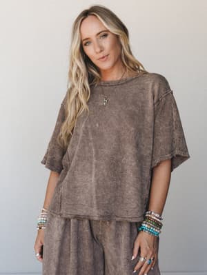A lived-in mineral-washed top in warm mocha, styled as a matching set and layered with stacks of beaded bracelets and a delicate charm necklace — the kind of effortless that looks like you weren't trying but absolutely were.