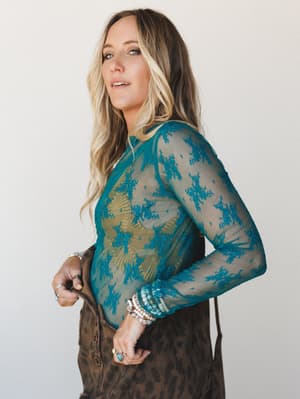 A sheer teal lace long-sleeve top layered over a bralette is styled with a brown leopard button-front skirt, stacked bracelets, and rings — the kind of outfit that looks effortless but is absolutely intentional.