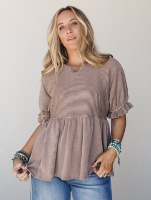 A relaxed peplum top in warm acorn brown with a subtle ribbed texture, styled with wide-leg jeans and stacked turquoise bracelets — the kind of effortless outfit that looks like you tried just enough.