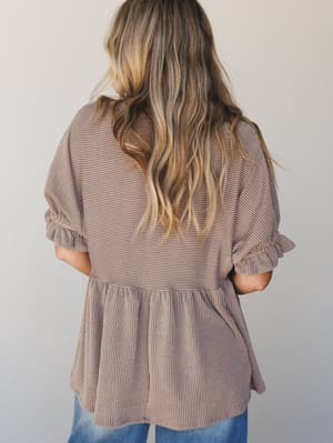 Shot from the back, this textured peplum top in a warm acorn brown pairs effortlessly with denim — the ruched sleeves and gathered waist seam do all the quiet, intentional work.