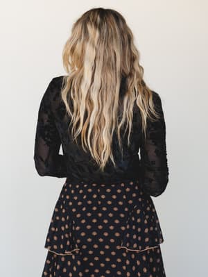 Shot from behind, this look pairs a sheer black floral burnout long sleeve top with a tiered black midi skirt in a warm sun print — dark, romantic, and quietly editorial.