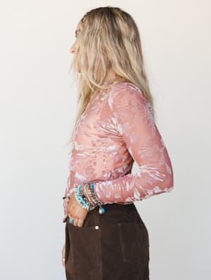 A side-profile shot of a model in a sheer dusty rose floral burnout top paired with dark chocolate suede pants, layered turquoise and silver bracelets adding that perfect lived-in boho finish.