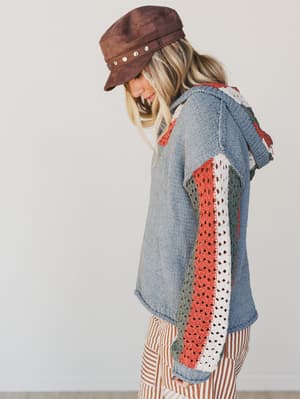 Woman wearing a denim jacket with colorful patchwork design and a brown hat.
