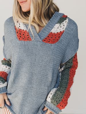Person wearing a blue sweater with colorful crochet details on a plain background