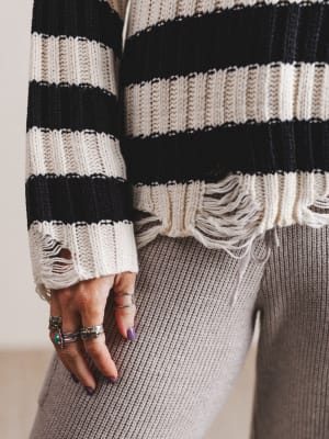 Close-up of a person wearing a black and white striped sweater with frayed cuffs.