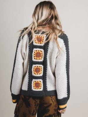 Person wearing a crochet cardigan with sunflower pattern on a plain background