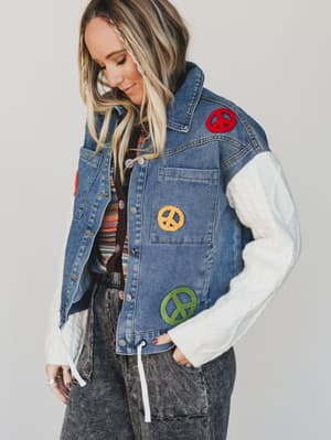 Person wearing a denim vest with peace symbol patches on a plain background