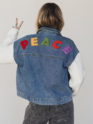 Person wearing a blue denim vest with colorful 'PEACE' letters on a plain background