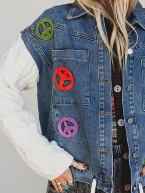 Denim jacket with peace sign patches on a plain background