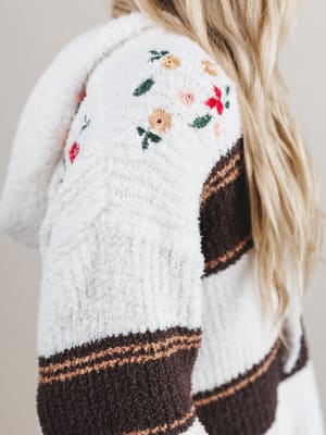 White cardigan with floral embroidery and brown accents on a neutral background