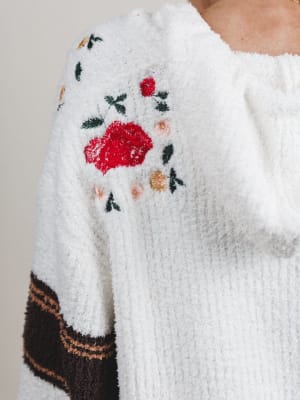 Close-up of a white sweater with floral embroidery on a neutral background