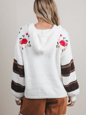 White sweater with floral patterns on sleeves worn by a person against a neutral background