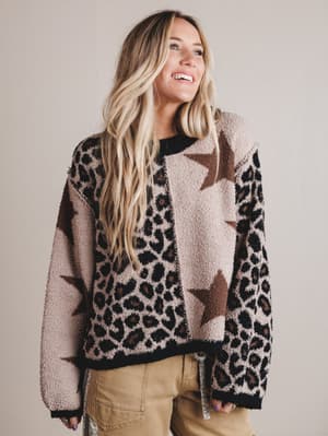 Woman wearing a patterned sweater with stars and leopard print on a plain background