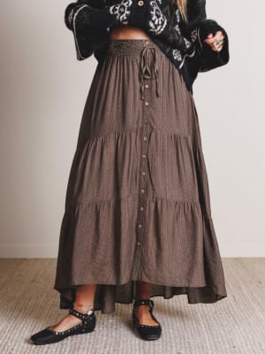 Person wearing a long brown tiered skirt with a plain background