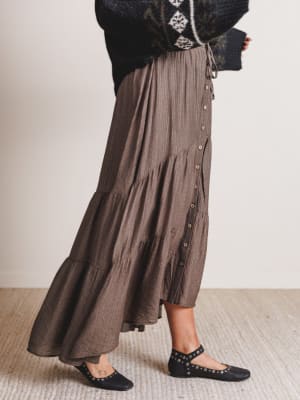 Person wearing a long brown skirt with a plain background
