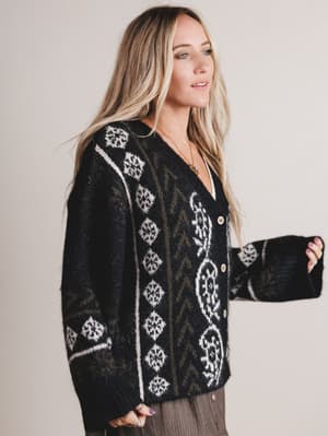 Woman wearing a black cardigan with white pattern on a plain background