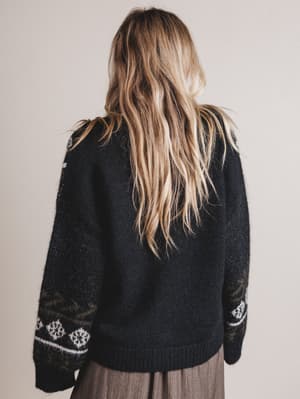 Person wearing a black sweater with white patterns on a plain background