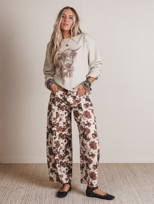 Woman wearing a sweatshirt with a graphic design and patterned pants against a plain background