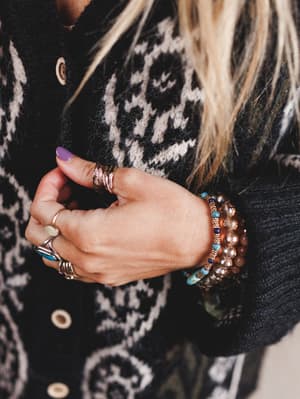 Close-up of a person's hand wearing multiple rings and bracelets against a patterned sweater background.