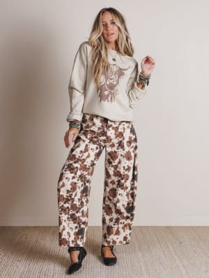 Woman wearing a sweatshirt with a graphic design and floral pants against a plain background