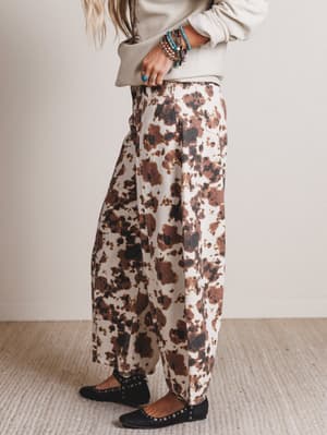 Person wearing floral-patterned pants and a beige sweater on a plain background