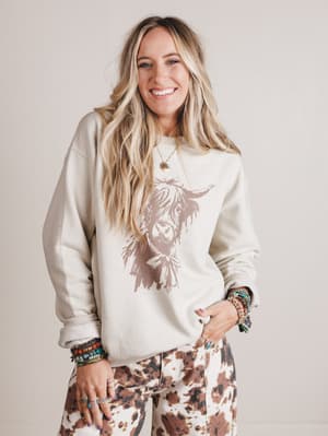 Woman wearing a white sweatshirt with a graphic design on a plain background