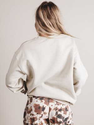 Person wearing a white sweater and patterned pants on a plain background