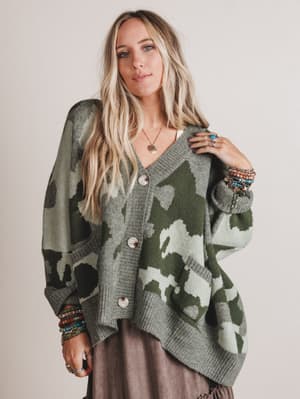 Woman wearing a camouflage-patterned cardigan against a plain background