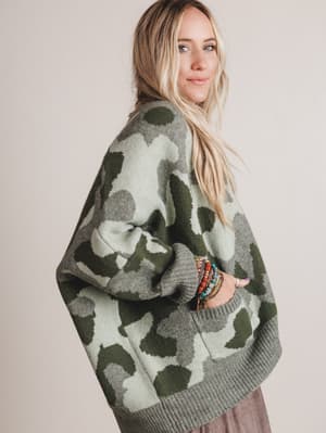 Woman wearing a camouflage-patterned sweater against a plain background