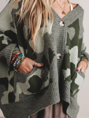 Person wearing a camouflage-patterned cardigan with colorful bracelets on a neutral background