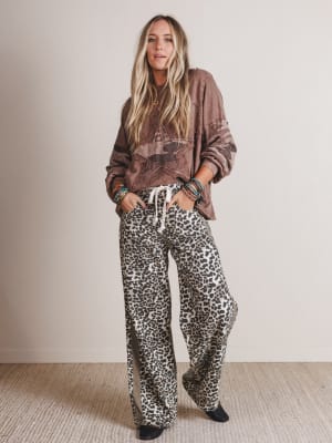 Person wearing a brown oversized hoodie and leopard print pants against a plain background