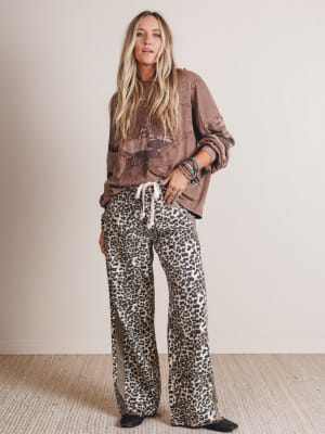 Woman wearing a brown jacket and leopard print pants against a plain background