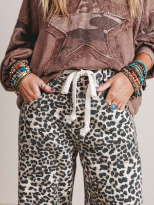Person wearing a brown star-patterned hoodie and leopard print pants with colorful bracelets.