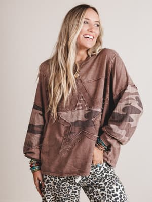 Woman wearing a brown oversized sweater with star design and leopard print pants on a plain background
