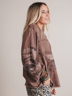 Woman wearing a brown sweater with camouflage patterns on a plain background