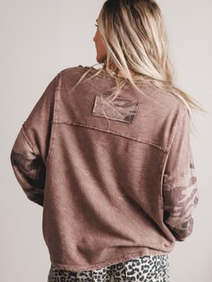 Person wearing a brown sweater with a patch on the back against a plain background