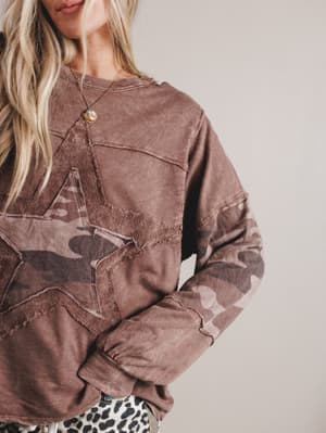 Brown sweater with star design worn by a person on a plain background