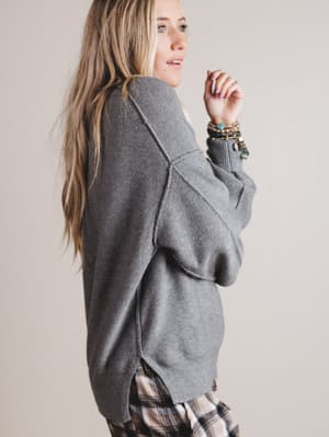 Woman wearing a gray sweater and plaid pants against a plain background