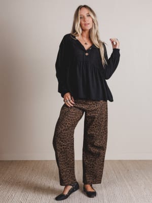 Woman wearing a black top and leopard print pants against a plain background