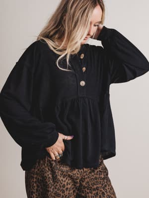 Woman wearing a black long-sleeve top with buttons and leopard print pants against a plain background