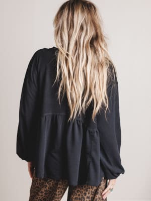 Person wearing a black top with long hair and leopard print pants on a plain background