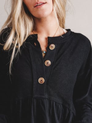 Close-up of a person wearing a black dress with buttons, focusing on the neckline.