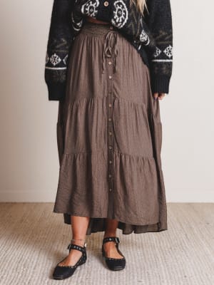 Person wearing a brown tiered skirt and black patterned sweater on a neutral background