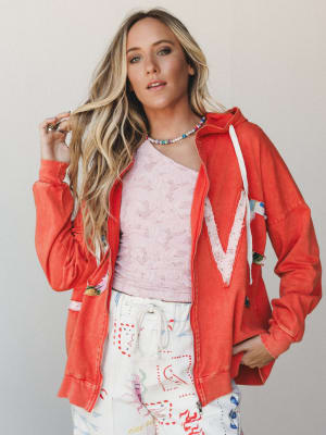 A relaxed, color-happy outfit built around a washed coral zip-up hoodie with a lace chevron appliqué — layered over a pink lace top and printed drawstring pants, with a beaded pearl necklace tying it all together in the most effortlessly playful way.