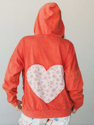 The back of a washed coral hoodie sweatshirt with a large heart-shaped floral fabric patch appliquéd at center back — the kind of piece that feels personal, like someone made it just for you.