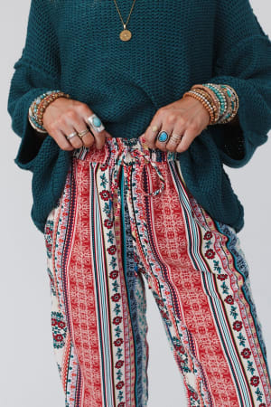 Model in The Nest Staycation Wide Leg Drawstring Pant in Red Clay, styled with beaded bracelets and turquoise rings, shown from mid-torso to knees.