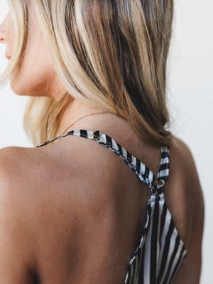 A close-up back detail shot of a black and white striped top with crossed adjustable straps and gold hardware — the kind of piece that looks just as good at a sleepover as it does on a coffee run.