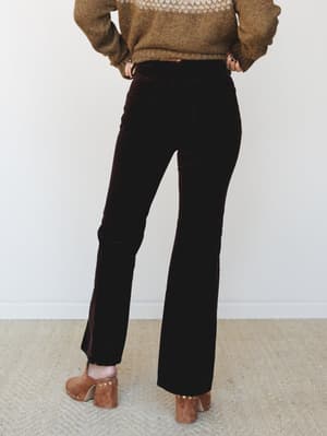 Shot from behind, a model pairs deep chocolate velvet flare trousers with a heathered olive fair isle sweater and studded suede block-heel mules — the whole look reads like a cozy fall Saturday that somehow got really good.